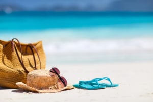 A bag, hat, sunglasses, and flip-flops on the beach.