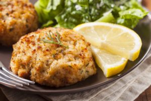 A plate of crab cakes with lemon wedges and salad.