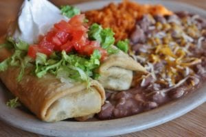 chimichanga covered in lettuce, tomatoes, and sour cream served with refried beans and rice